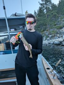 An angler displaying a freshly caught trout while fishing from a boat in a scenic lake environment.