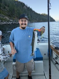 Angler proudly displaying a caught trout while fishing on a boat surrounded by scenic forested hills.