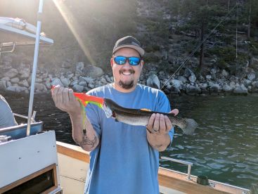 Angler proudly displaying a Rainbow Trout caught while fishing from a boat in a scenic lake environment.