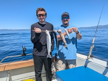 Two anglers proudly displaying their catch of Lake Trout while fishing on a sunny day at Lake Tahoe.