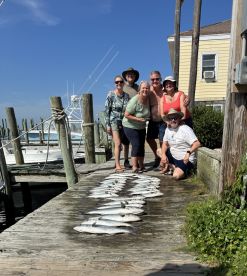 A group of six anglers proudly posing with their catch of fish displayed on the dock after a successful fishing trip.