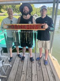 Three anglers proudly displaying their catch of fish on a personalized board at a dock, showcasing a successful day of fishing.