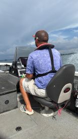 A person seated at the helm of a fishing boat, navigating through open waters, showcasing the boat's interior and control panel.