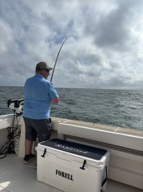 An angler actively reeling in a catch while fishing from a boat in open waters, showcasing the excitement of the sport.