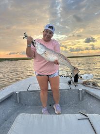 Angler proudly displaying a large Redfish against a stunning sunset backdrop while on a fishing trip.