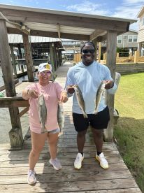 Two anglers proudly displaying their catch of Speckled Trout on a dock after a successful fishing trip.