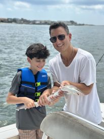 A young boy and his father joyfully holding a small shark while fishing on a boat, showcasing a memorable family fishing experience.