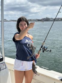 A young angler proudly displaying her catch of two fish while fishing from a boat, showcasing a sunny day on the water.