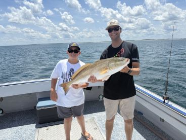 A young angler and an adult proudly display a large Redfish aboard a fishing charter in open waters.