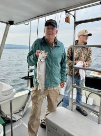 An angler proudly displaying a large Lake Trout aboard a fishing boat, showcasing a successful day on the water.