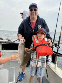 A proud moment as a young boy and his father display a freshly caught Lake Trout aboard their fishing boat.