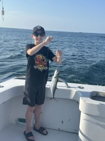A young angler proudly displaying a Spanish Mackerel while fishing on a boat in open waters.