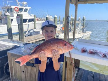 A young angler proudly displaying a large Red Snapper at the dock after a successful fishing trip.