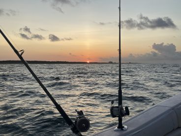 A serene sunset view from the side of a fishing boat, showcasing fishing rods against the backdrop of a tranquil ocean.