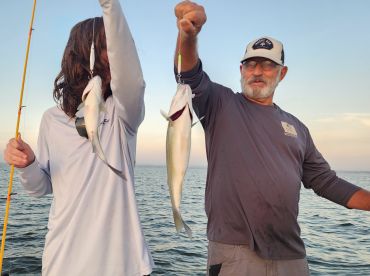 A young angler and an adult proudly displaying their catches while fishing on a calm waterway during sunset.