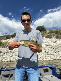 A young angler proudly displaying a freshly caught Largemouth Bass while fishing from a boat on a sunny day.