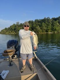 An angler proudly displaying a large striped bass while fishing on a calm lake, showcasing a beautiful morning fishing environment.