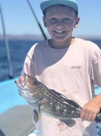 Young angler proudly holding a colorful Spotted Grouper while fishing on a boat in clear blue waters.