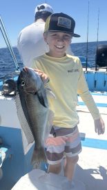 Young angler proudly holding a large fish while fishing on a boat, showcasing a sunny day at sea.