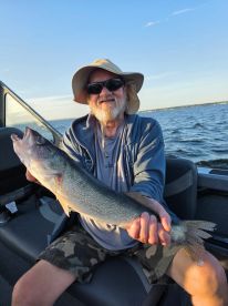 An angler proudly displaying a sizable Walleye while fishing on a boat during a sunny day.