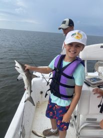 A young angler proudly displaying a caught shark while fishing on a boat, showcasing a fun day on the water.