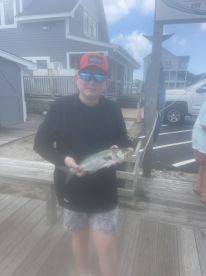 A young angler proudly displaying a caught fish at the dock, with a coastal fishing environment in the background.