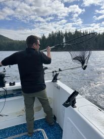 Angler skillfully using a net to catch a fish while fishing in a scenic coastal environment surrounded by lush forests.