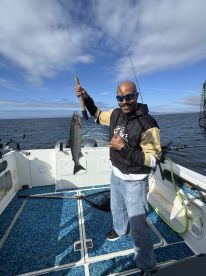 Angler proudly displaying a large fish on a boat during a fishing trip, with a scenic ocean backdrop.