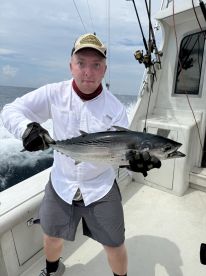 Angler proudly displaying a large Tuna aboard a fishing boat, showcasing a successful offshore fishing trip.