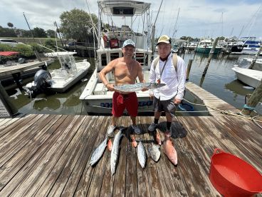 Two anglers proudly displaying their catch, including a large Barracuda and several Snapper, at the marina after a successful fishing trip.