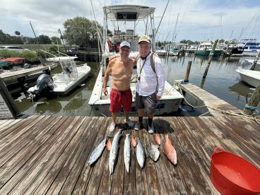Two anglers proudly displaying their catch of the day, including Mackerel and Snapper, at the dock after a successful fishing trip.