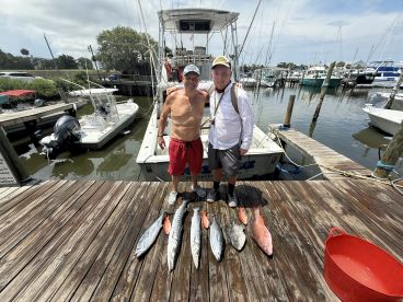 Two anglers proudly displaying their catch of Mahi Mahi and Snapper on the dock after a successful fishing trip.