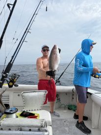 Angler proudly displaying a large Snapper while fishing on a charter boat in open waters.