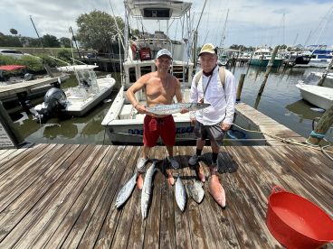 Two anglers proudly displaying their catch, including a large King Mackerel and several other fish, at the dock after a successful fishing trip.
