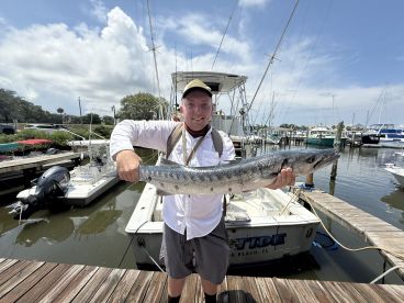 Angler proudly displaying a large Barracuda at the marina after a successful fishing trip.