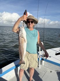 An adult angler proudly displaying a large Redfish while fishing on a charter boat in a coastal waterway.