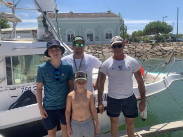 A family poses in front of their fishing charter boat at the dock, showcasing a sunny day and a relaxed atmosphere.