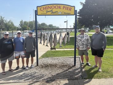 Group of anglers proudly posing by a catch board displaying several Chinook Salmon at Chinook Pier in Grand Haven, Michigan.