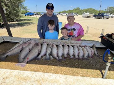 A family poses proudly behind a catch of catfish displayed on a cleaning table after a successful fishing trip.