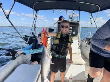 Two young anglers excitedly displaying their catch on a fishing boat, showcasing a large catfish during a family fishing trip.