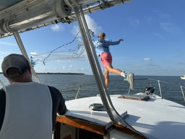 A young angler casting a net from the bow of a boat, showcasing an active fishing moment on calm waters.