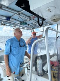 Two anglers navigating the boat's helm, enjoying a day on the water with clear skies and a calm sea.