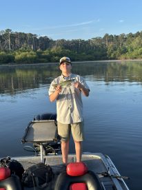 A young angler proudly displaying a Bass while fishing on a calm lake during early morning.