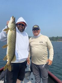 Two anglers proudly displaying a Northern Pike caught during a fishing trip on a serene lake.