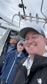 A family enjoying a fishing trip on a boat, with a young boy and two adults posing for a selfie in the cabin area.