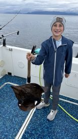 Young angler proudly holding a large stingray on a fishing boat, showcasing a successful catch during a fishing trip.