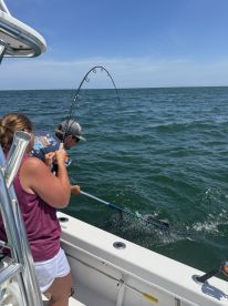 A young angler is reeling in a fish while another person prepares to net it, showcasing an exciting moment during a fishing trip on a boat.