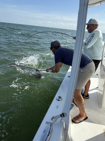 Two anglers actively fishing from a boat, with one preparing to net a fish in the water, showcasing the excitement of a fishing trip.