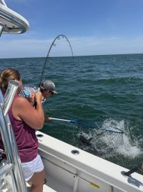 Anglers actively engaged in reeling in a fish while fishing from a boat in open water.