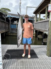 Young angler proudly holding a large King Mackerel at the dock, showcasing a successful fishing trip.
